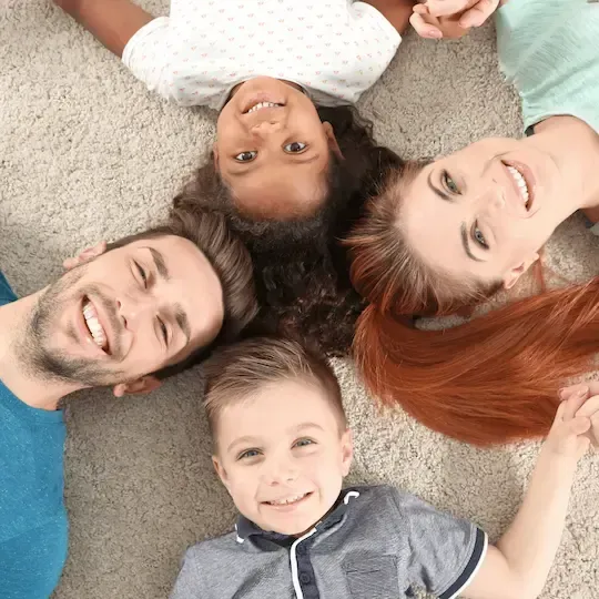 A family is laying on the floor in a circle and smiling.