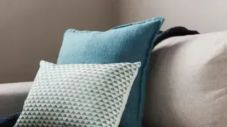 Two pillows, one teal, one with triangle pattern, on a light beige couch.