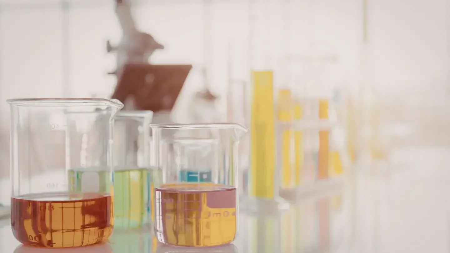 Laboratory glassware with colorful liquids. A microscope is in the background.