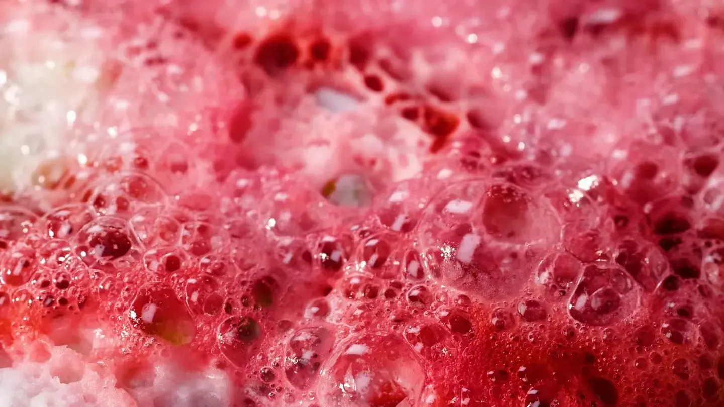 Close-up of pink red foam bubbles and frothy liquid surface
