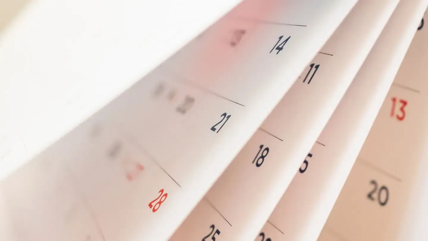 Close-up of a flipped wall calendar page with dates in black and red on white paper