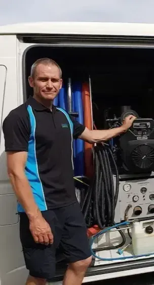 Kerry Walker of Advanced Carpet Cleaning Christchurch in a blue and black shirt is standing in front of a van.