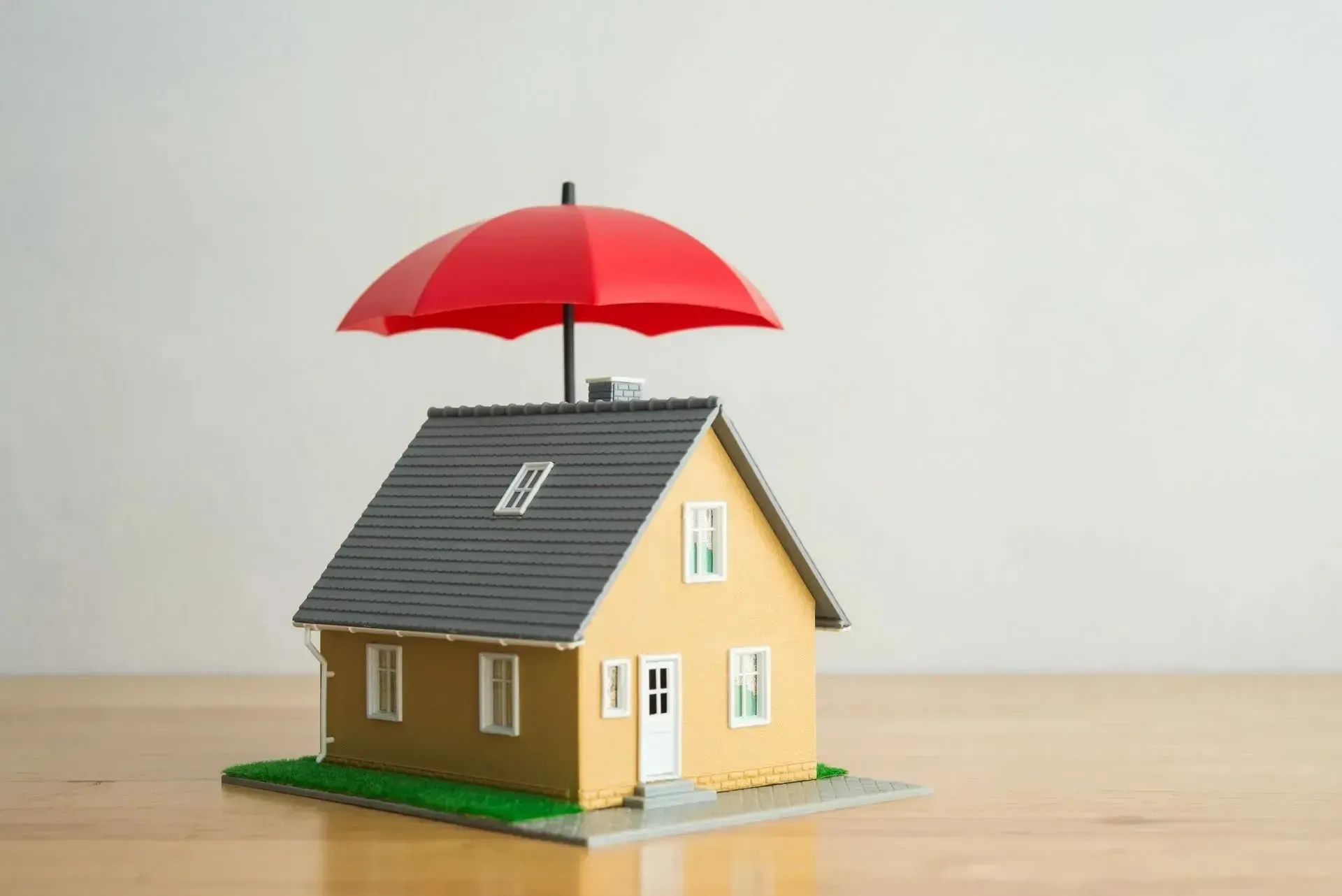 Small model house sheltered by a red umbrella, on a table.