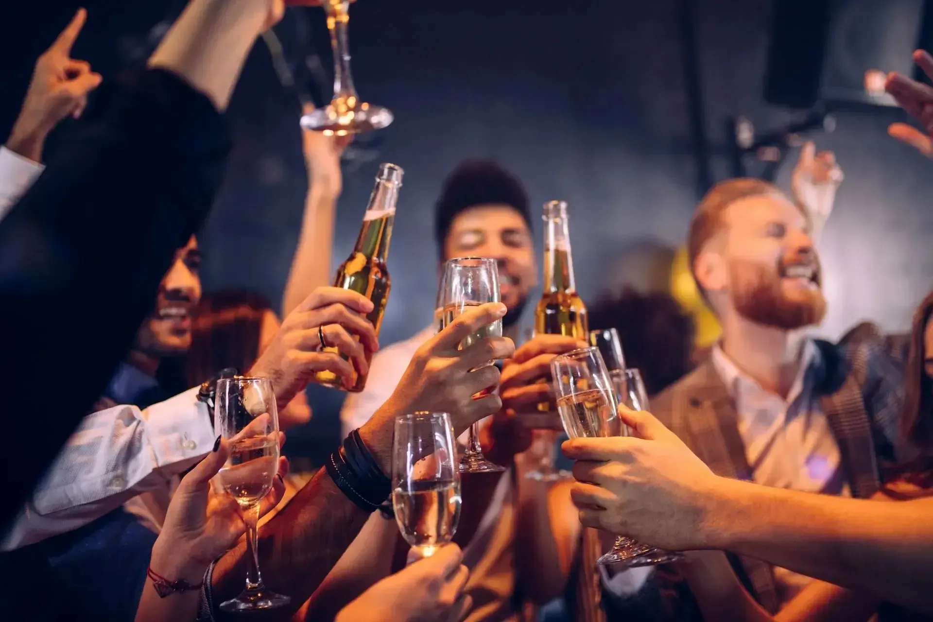People toasting with drinks at a party, celebrating, in a dimly lit space. Cheers and happy expressions.