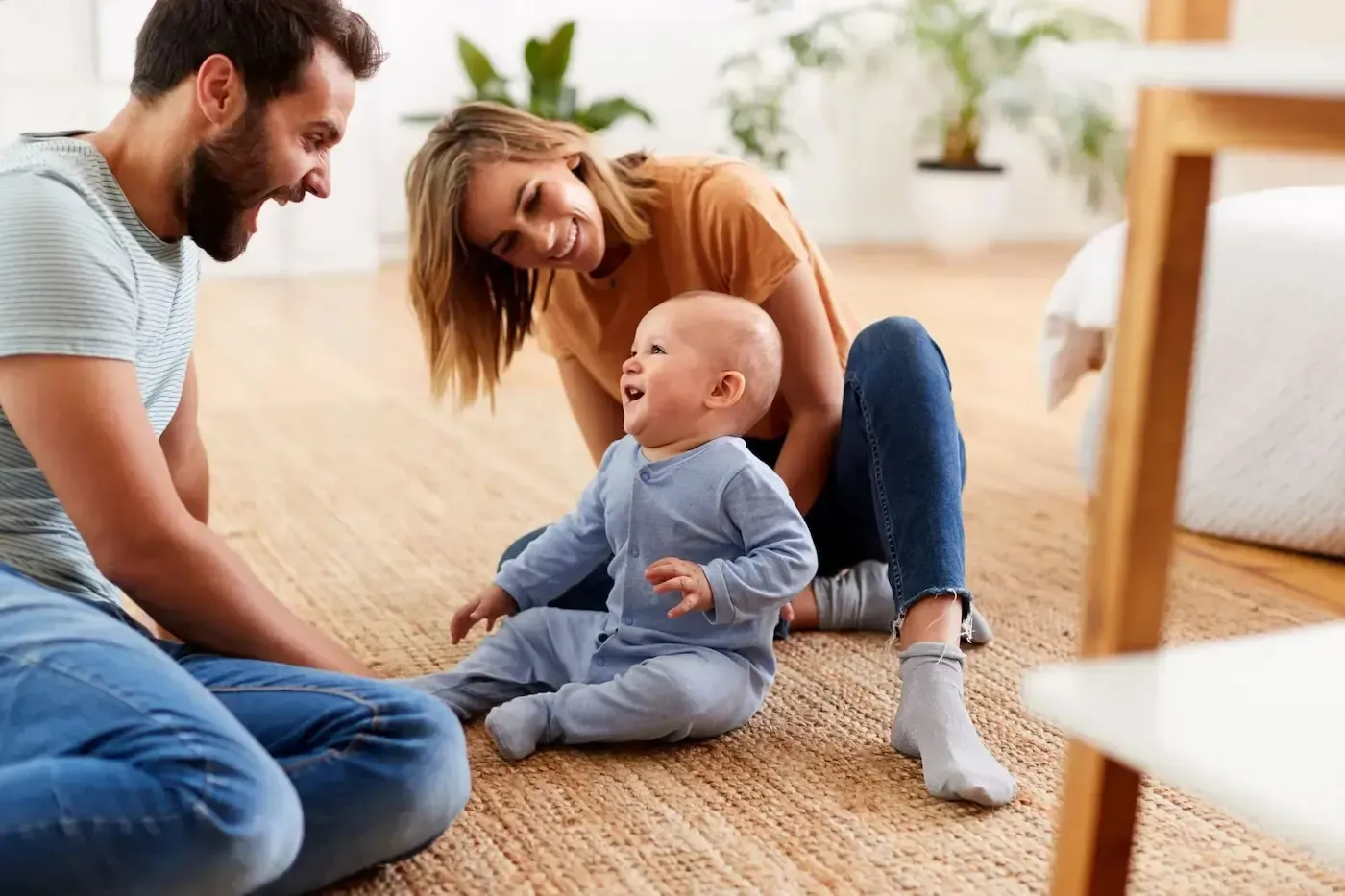 Parents play with smiling baby on home floor.