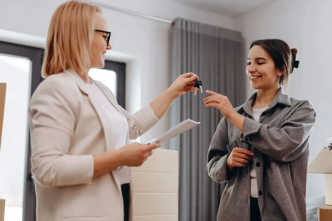 Woman hands keys in room with boxes, suggesting a move-in.