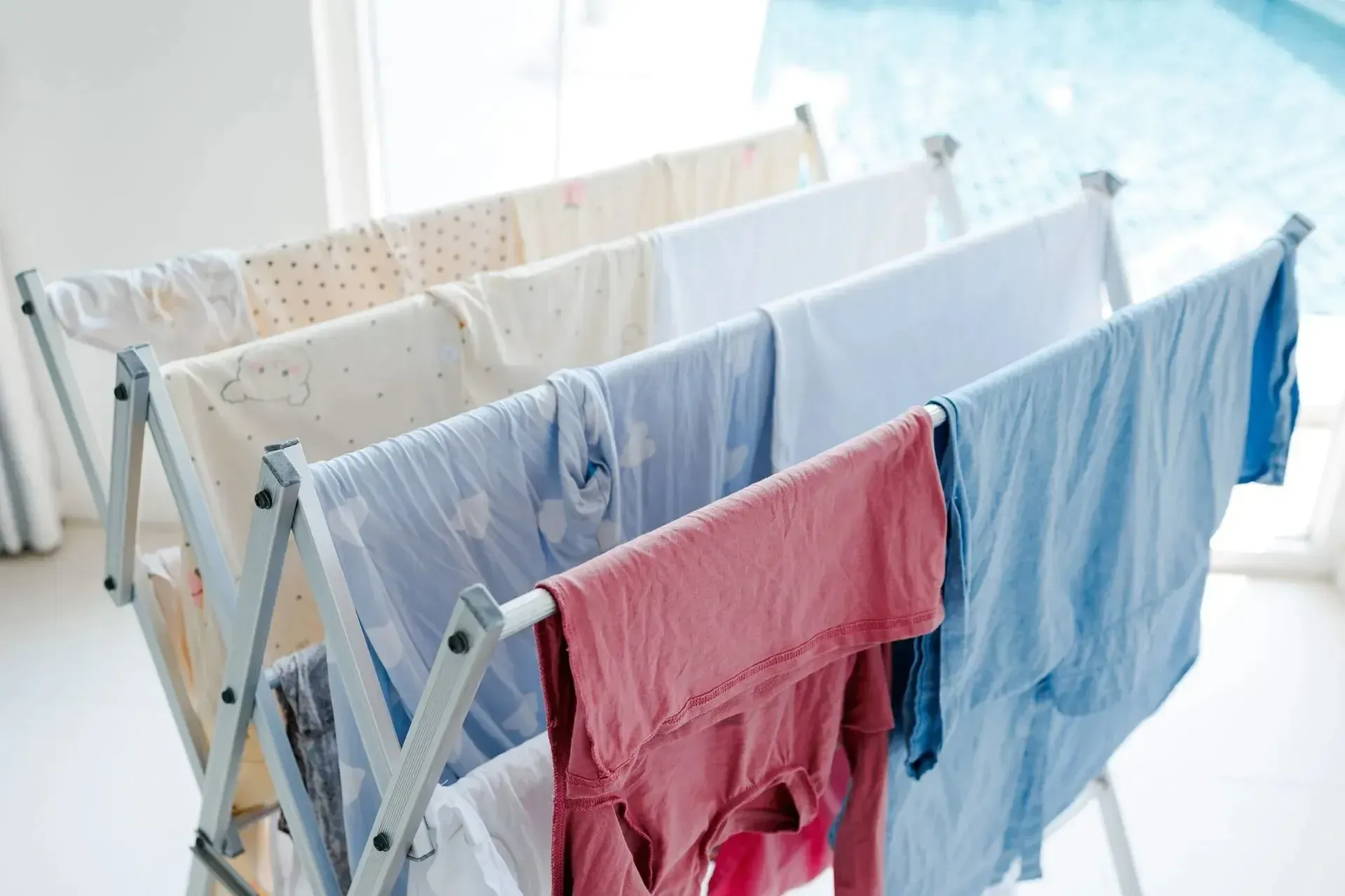 Clothes drying on a white folding rack indoors near a window. Various colors.