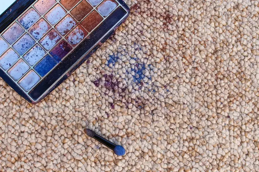 Makeup eyeshadow palette spilled on a textured beige rug.