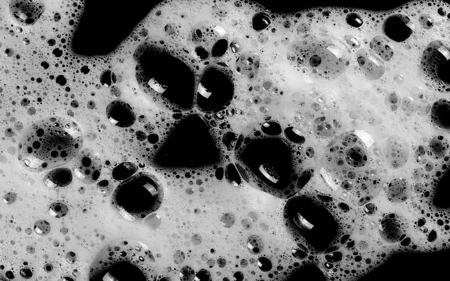 Black and white close-up of foamy liquid with dark bubbles and irregular spots