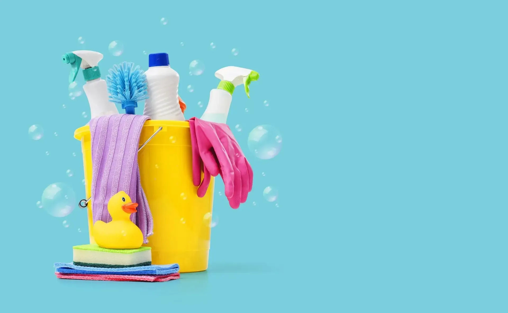 Yellow bucket filled with cleaning supplies: spray bottles, brush, cloths, and a rubber duck, against a blue background.
