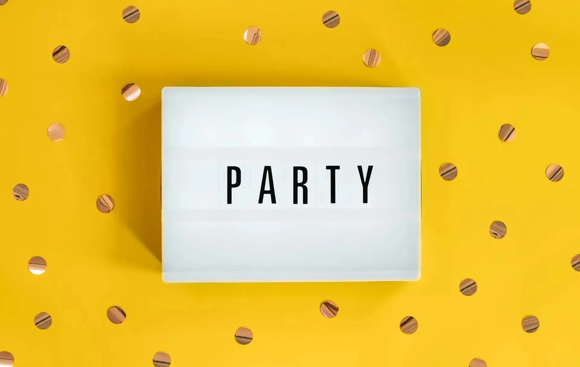 White lightbox sign on yellow confetti background reading “PARTY”