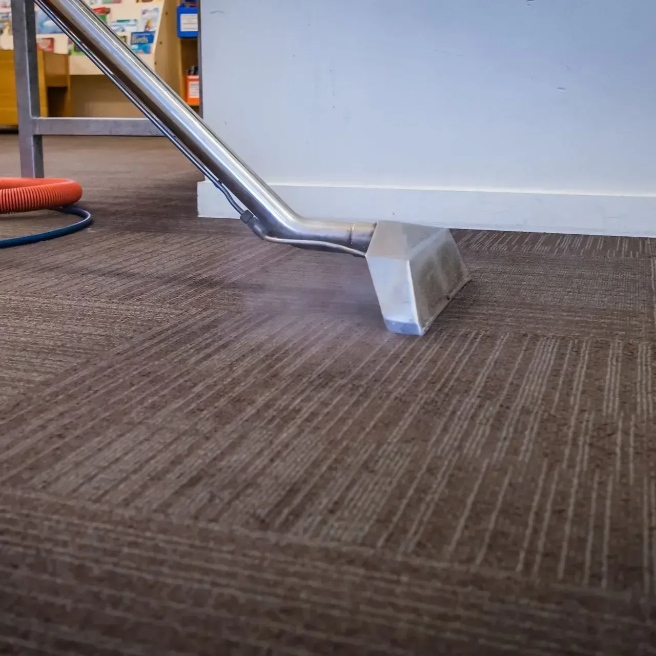 A vacuum cleaner is cleaning a brown carpet in a room.