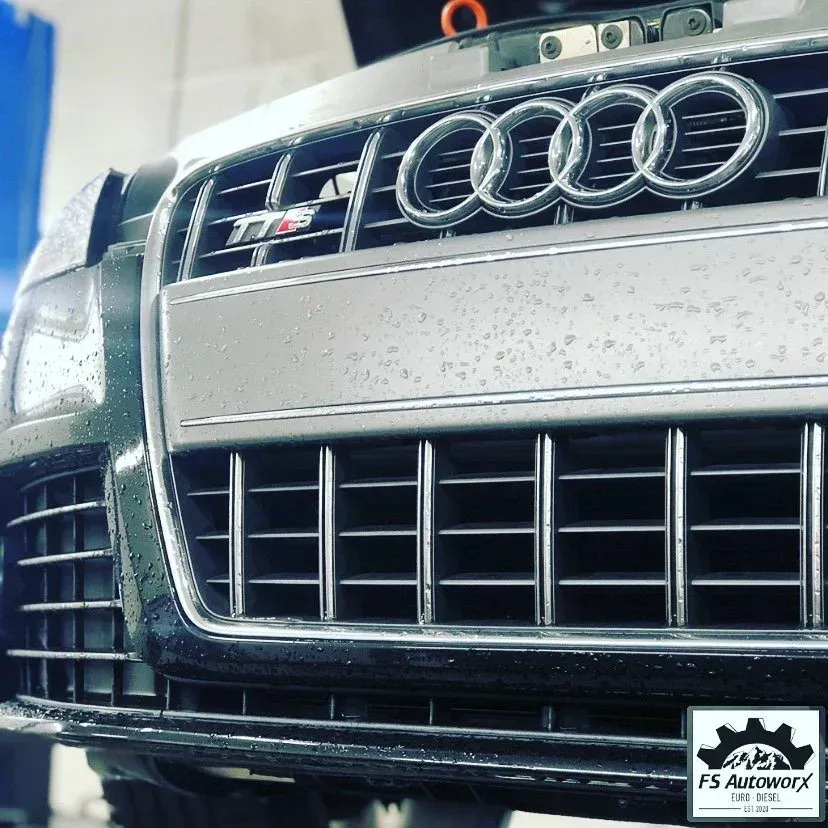 Close-up of a silver Audi front grille with S badge and raindrops at a car wash.