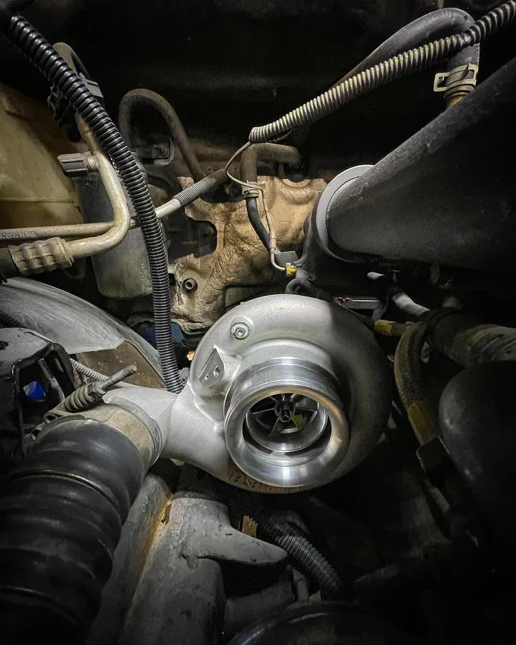 Close-up of a turbocharger mounted in an engine bay with hoses and wiring around it