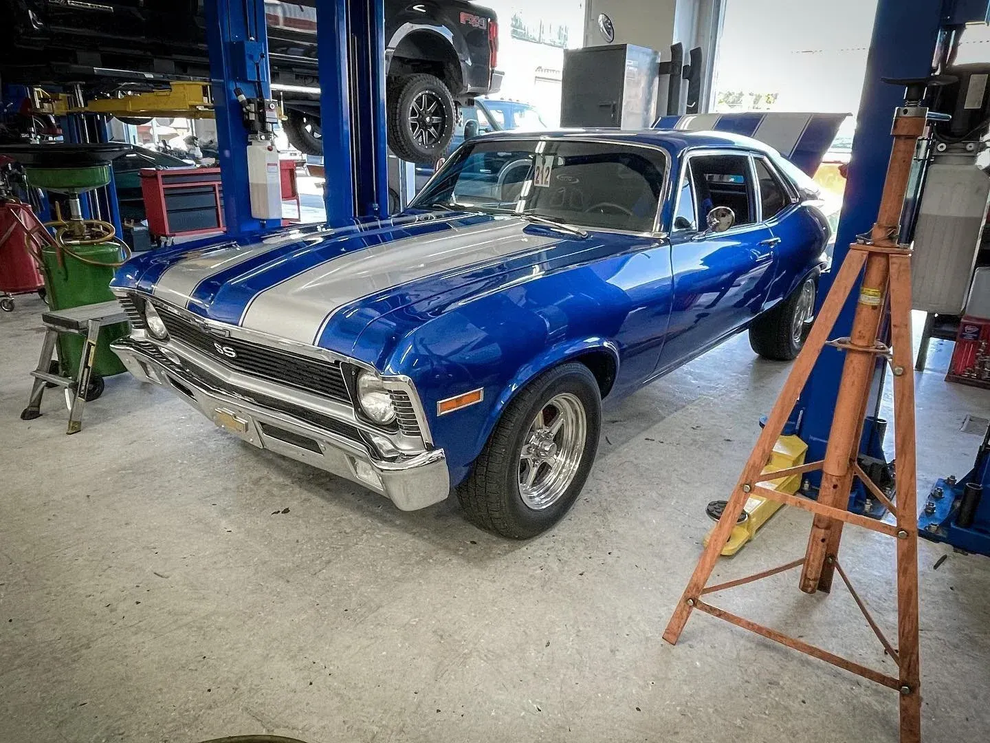 Blue classic muscle car with white racing stripes in a garage, raised on stands