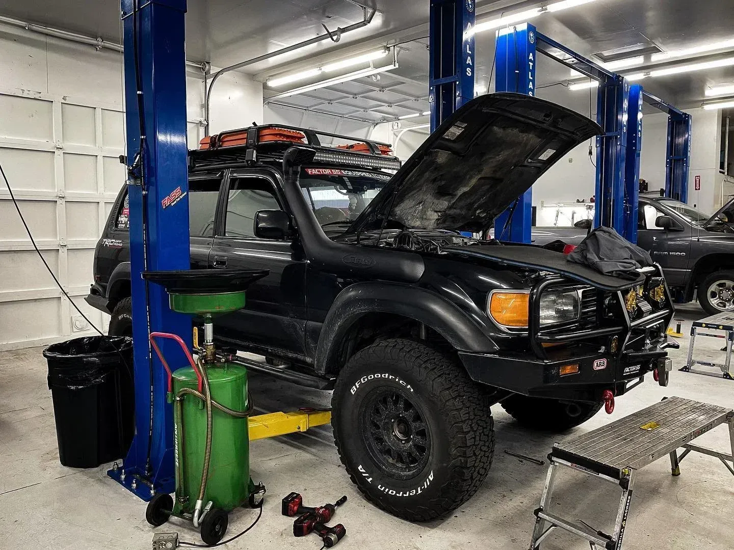 Black SUV with hood open on a lift in an auto repair shop, with tools and equipment nearby