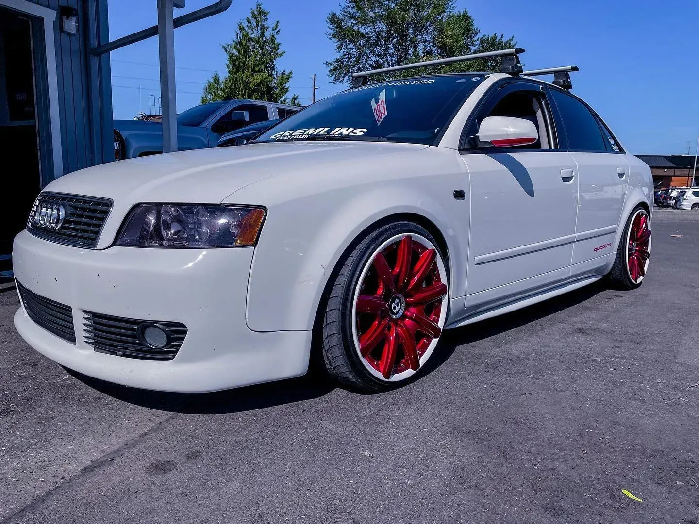 White sedan with red rims parked outdoors beside a blue building under a clear sky