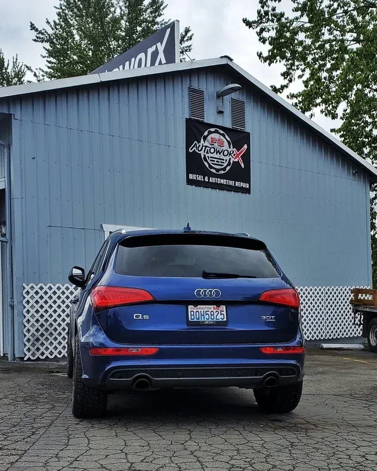Blue Audi SUV parked outside a gray building with a racing-style sign and a white lattice fence.