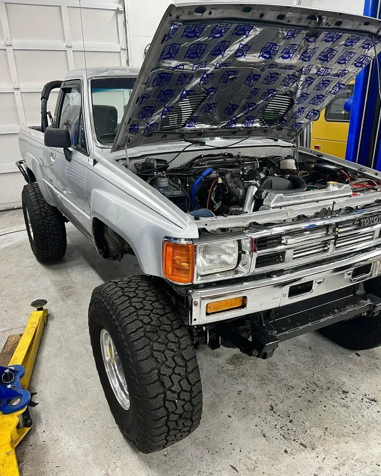 White lifted pickup truck in a garage with hood open, exposing the engine.