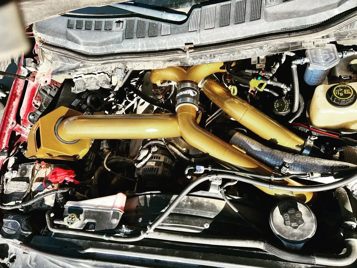 Close-up of a car engine bay with gold and black hoses and metallic components.