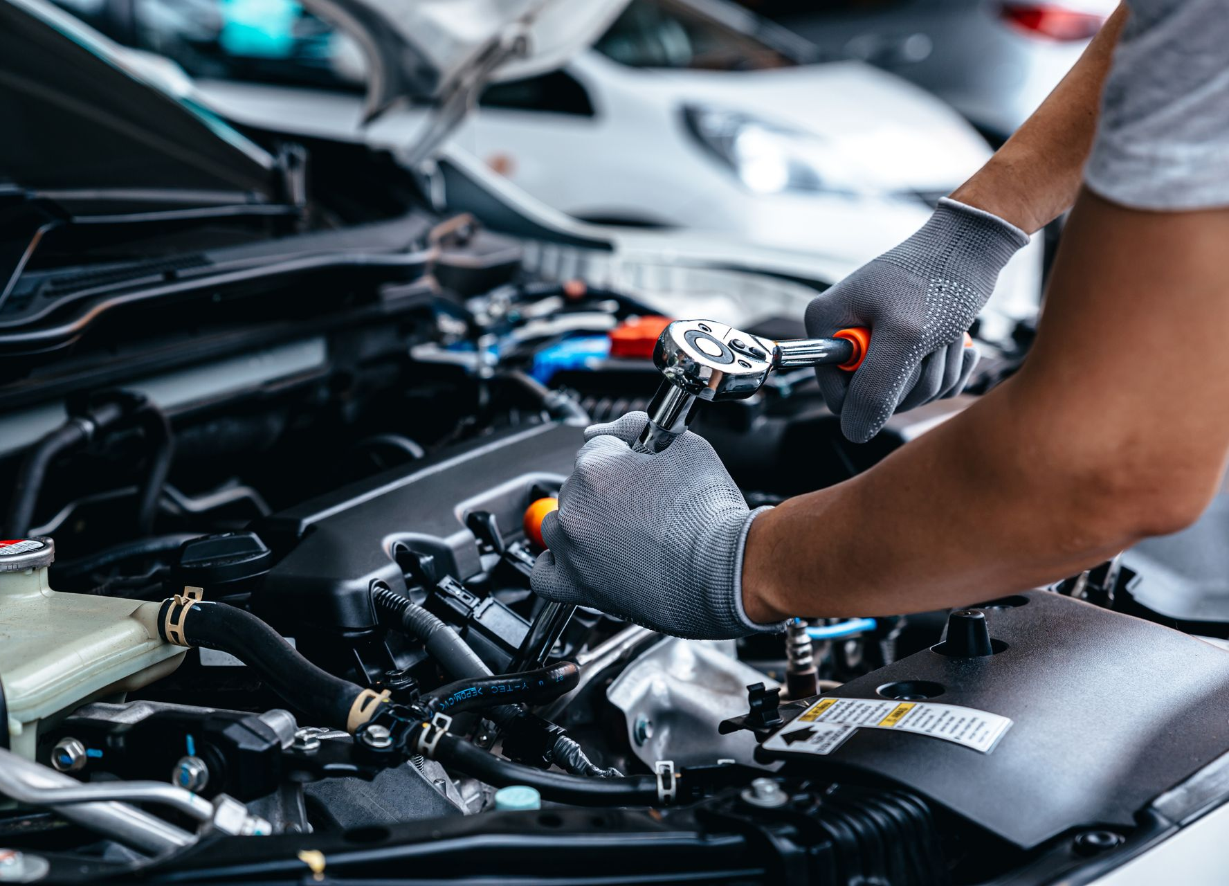 Mechanic using a wrench on a car engine under the hood, representing auto repair shop and diesel engine repair services