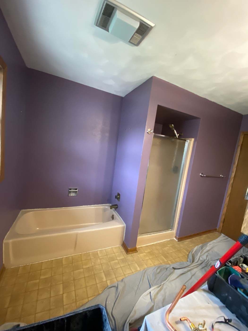 Purple-walled bathroom with a bathtub, shower, and tan tile floor. Construction tools are in the foreground.