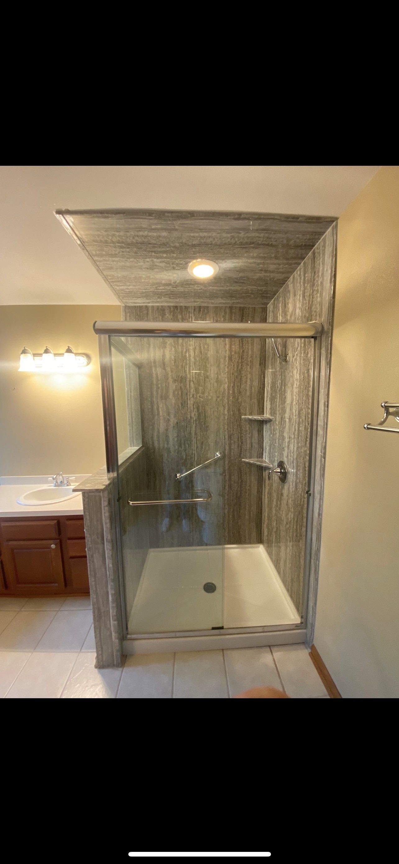 Bathroom shower with glass doors, gray tiled walls, and built-in shelves.