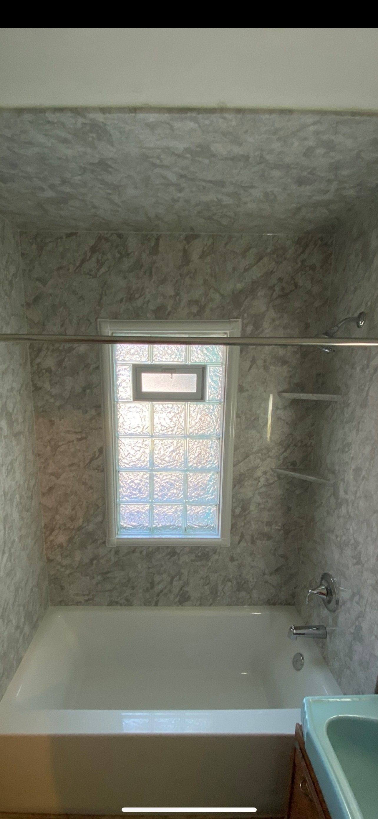 Bathroom with white tub, glass block window, gray walls, and shower curtain rod.