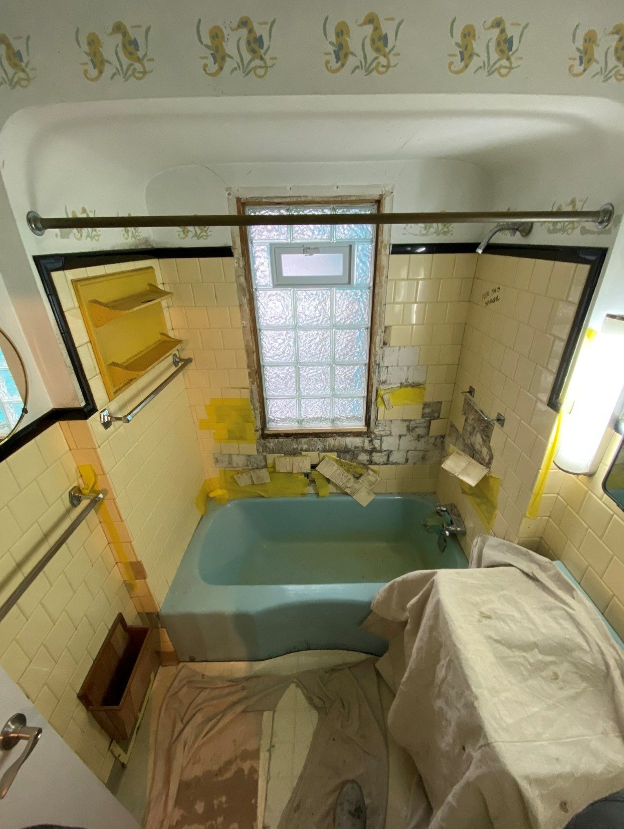 Bathroom with blue tub, yellow tiles, and demolition in progress.