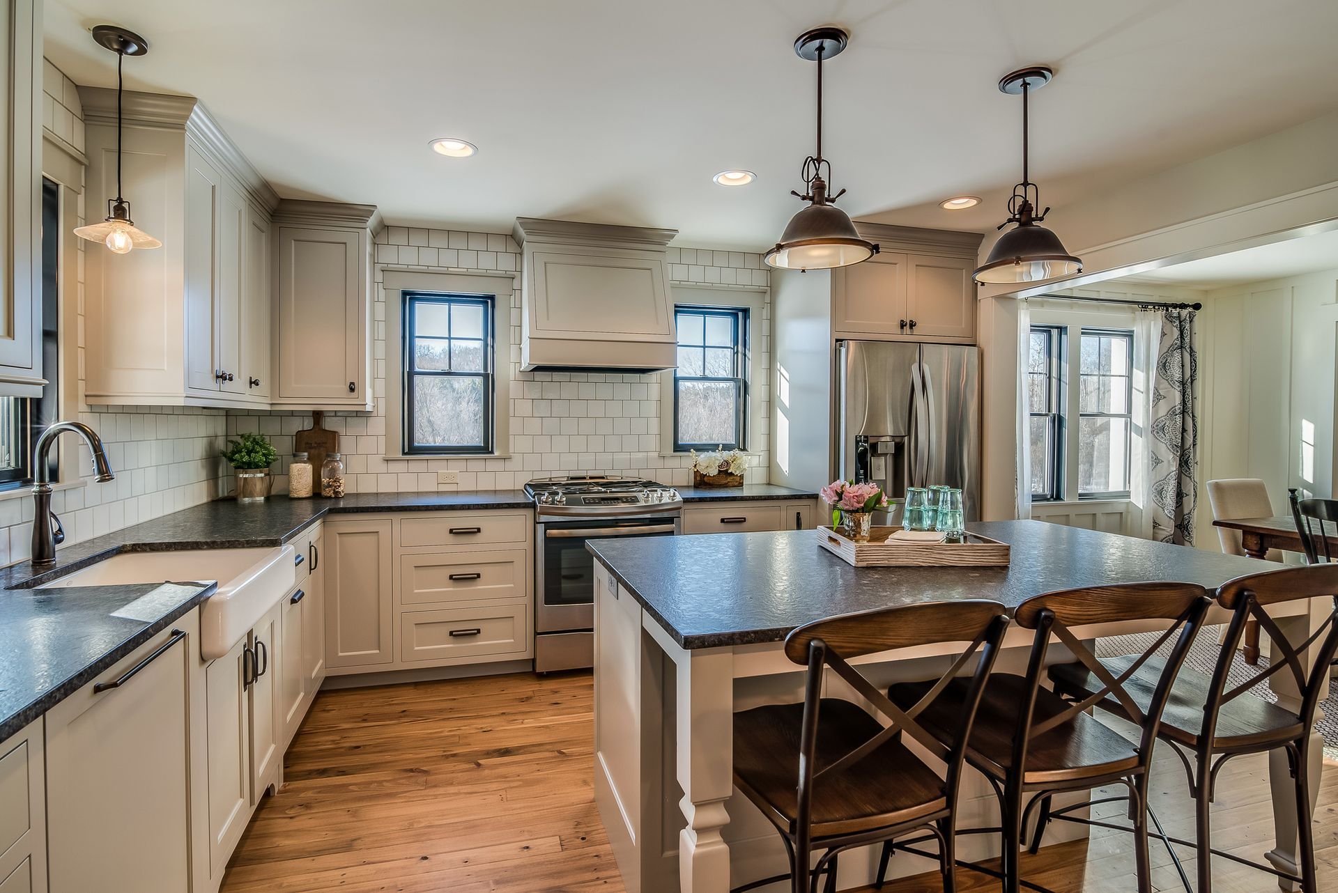 Spacious kitchen with white cabinets, dark countertops, a large island with seating, and wooden floors.