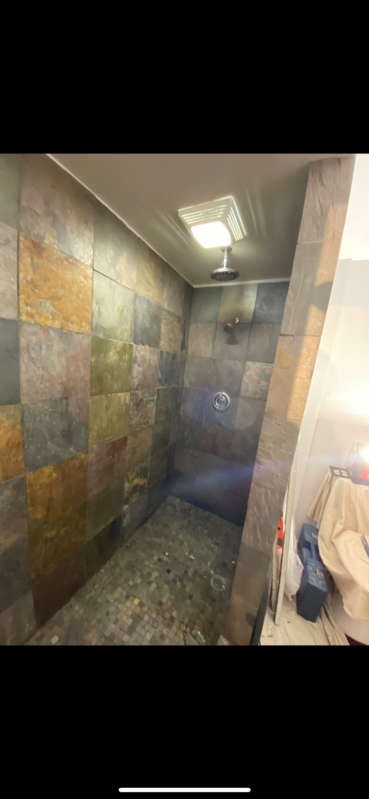 Shower stall with stone tile walls, pebble floor, and a mounted showerhead.