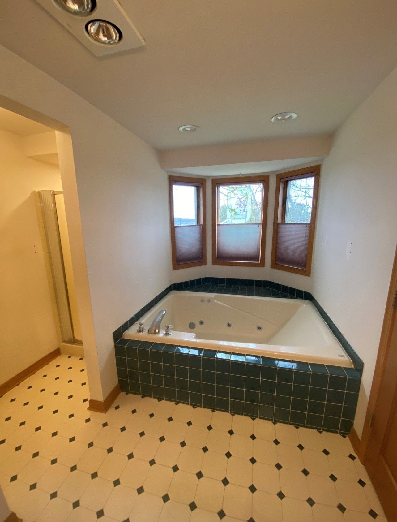 Bathroom with a corner jacuzzi tub, windows, and black and cream tile flooring.