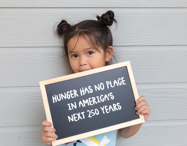 Child holding a black sign that reads, “Hunger has no place in America’s next 250 years.”