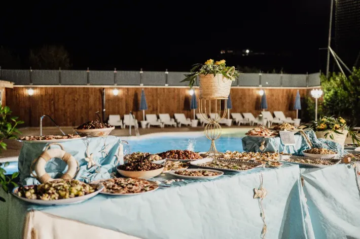 Tavolo da buffet con vari cibi accanto a una piscina di notte.
