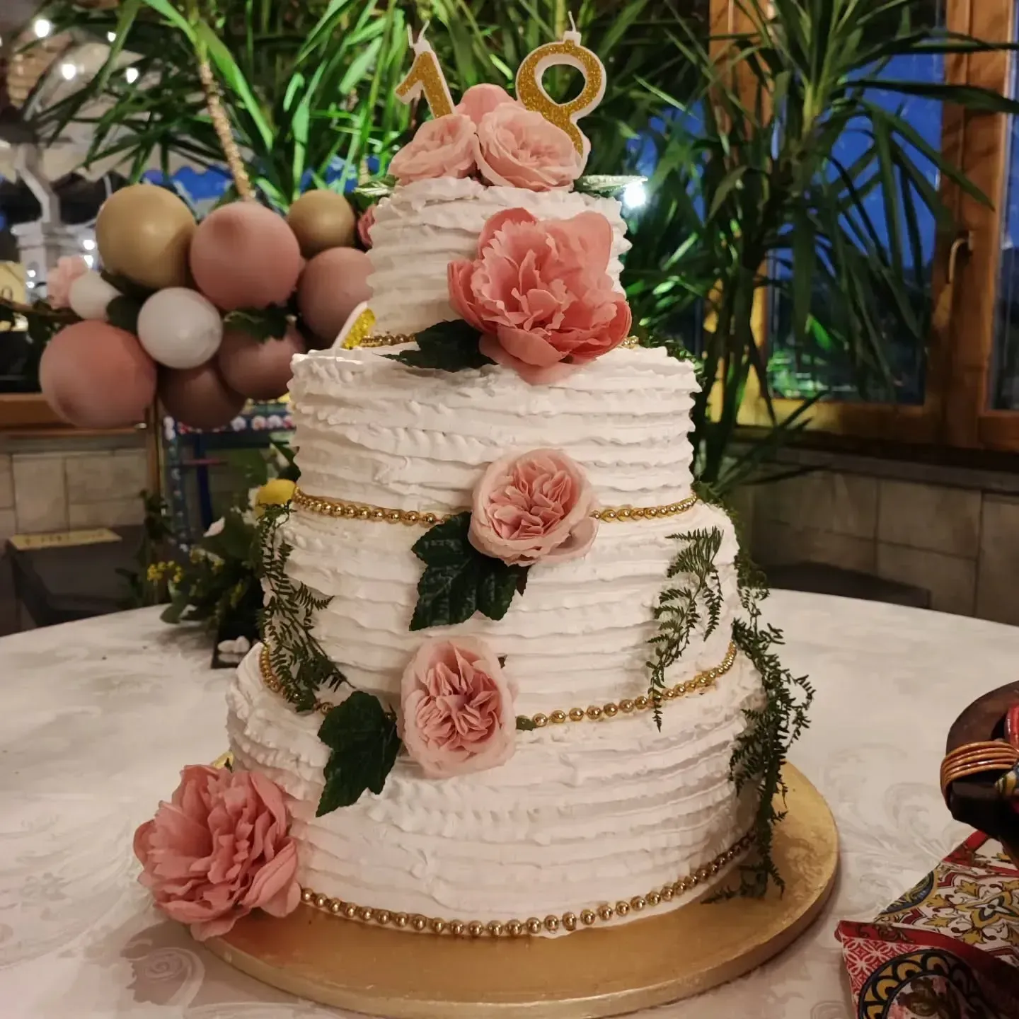 Torta a tre piani glassata di bianco, decorata con fiori rosa, verde e una candela con la scritta