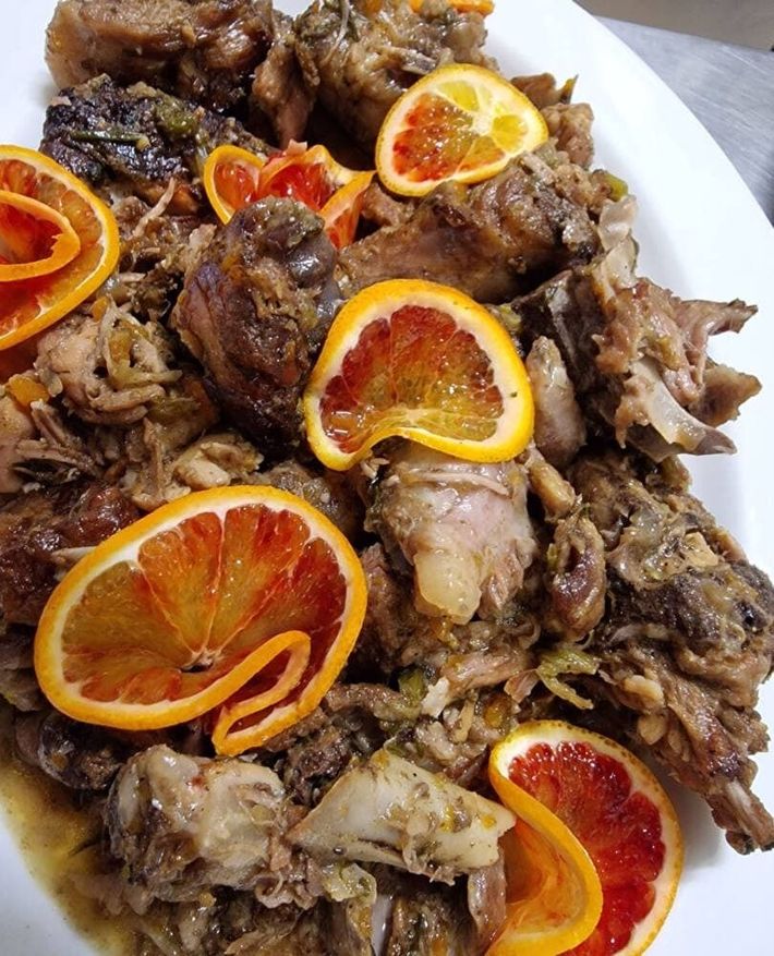 Piatto di carne cotta, guarnito con fette di arancia rossa su un piatto bianco.
