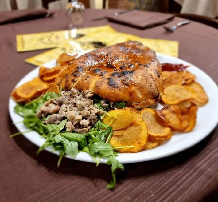 Calzone su un piatto con verdure, patatine dolci e un contorno di carne; ambiente da ristorante.