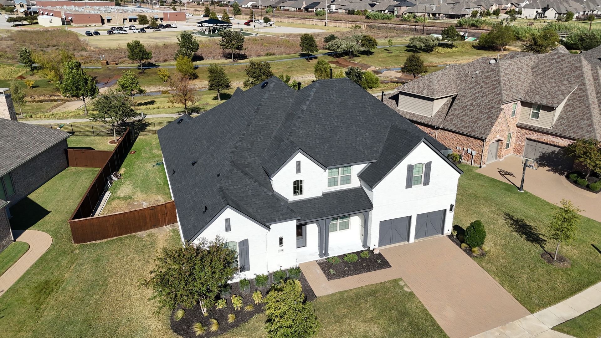 Aerial view of a white two-story suburban house with a dark roof and driveway in a neighborhood.
