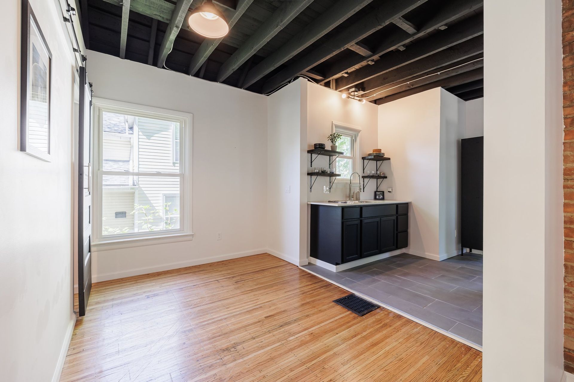 An empty room with hardwood floors , a sink , and a window.