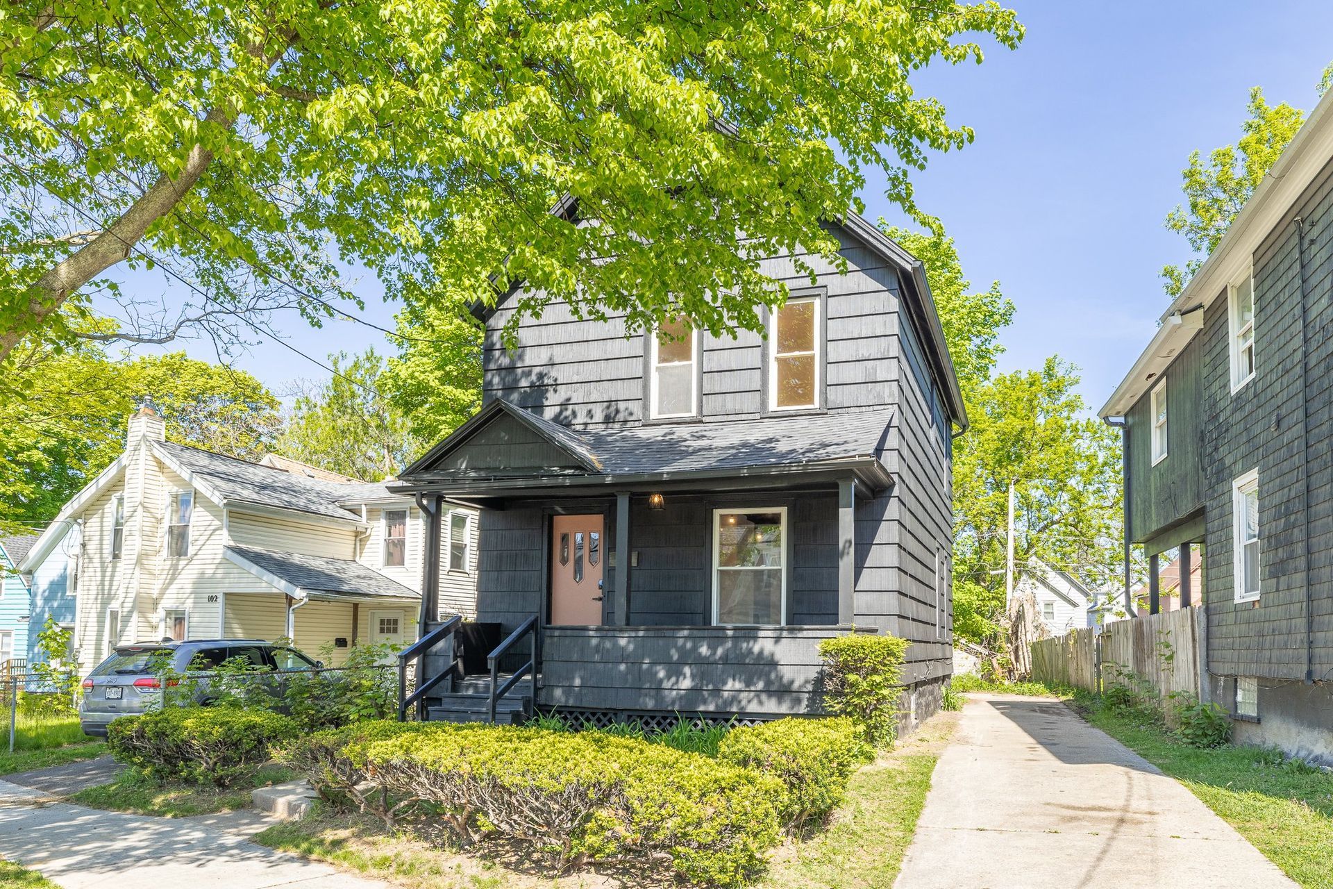 A black house with a porch and a car parked in front of it.