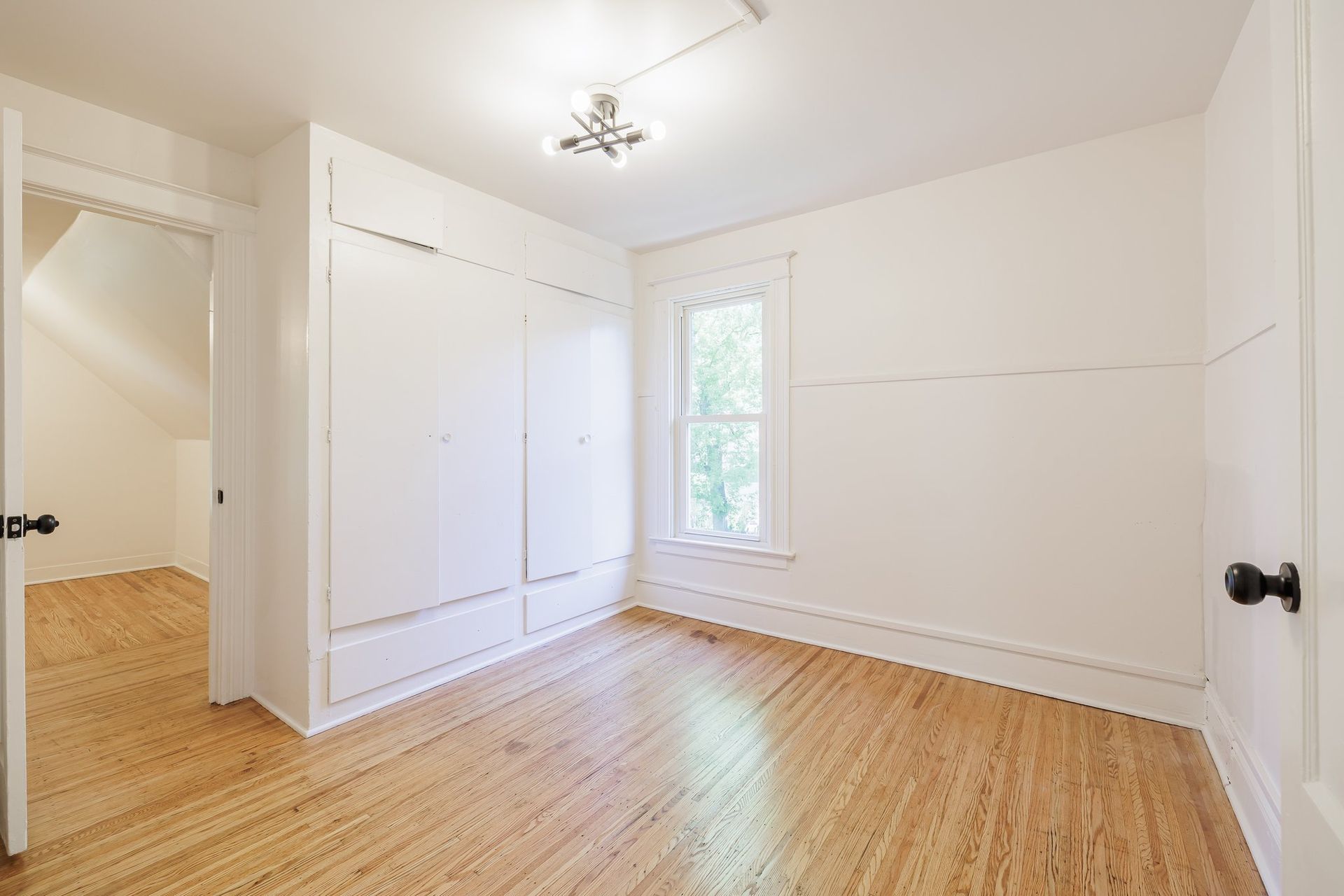 An empty bedroom with hardwood floors and white walls.