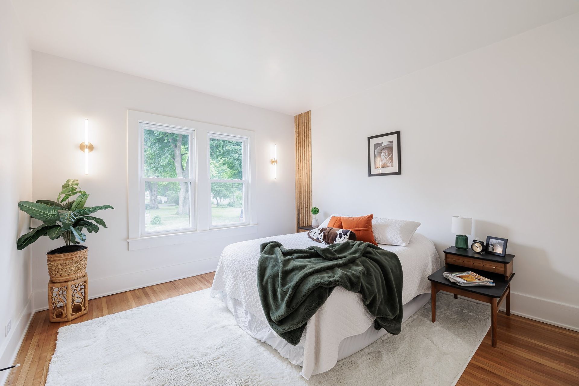 A bedroom with a bed , nightstand , and plant.