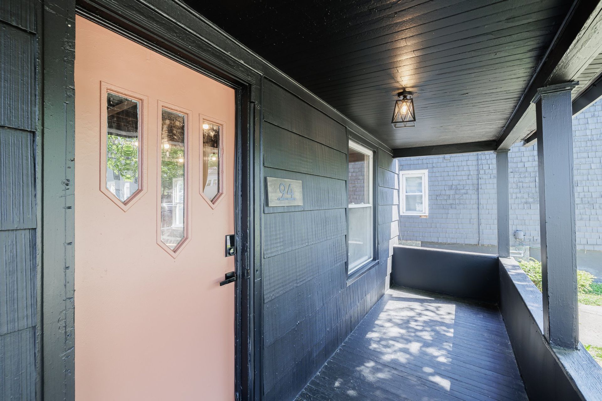 A black house with a pink door and a porch.