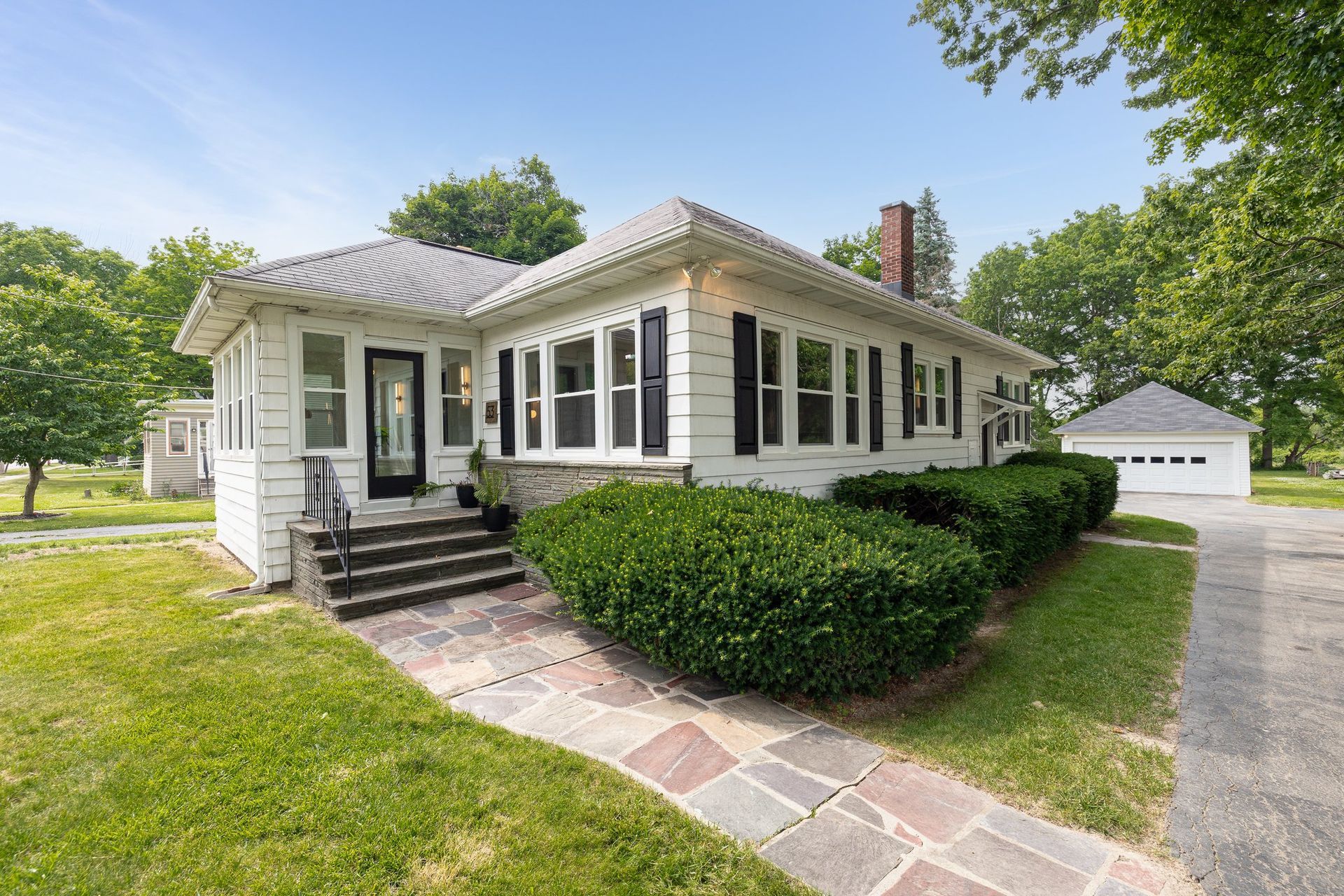 A white house with black shutters is sitting on top of a lush green field.