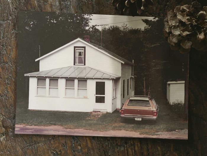 A picture of a white house with a red car parked in front of it