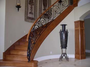 A wooden staircase with a wrought iron railing and a vase on a stand.