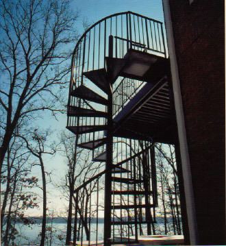 A spiral staircase leading up to a balcony overlooking a body of water