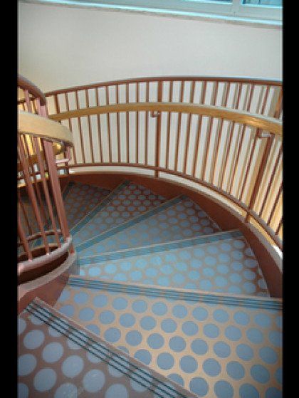 A spiral staircase with a wooden railing and a patterned floor