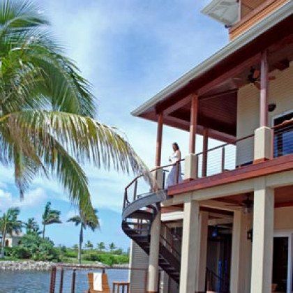A woman in a white dress stands on a balcony overlooking a body of water