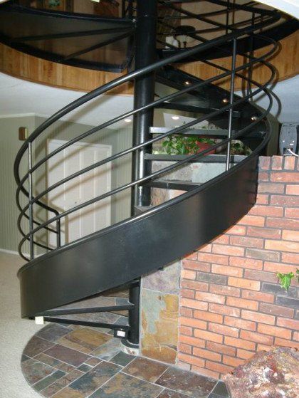 A black spiral staircase with a brick wall in the background